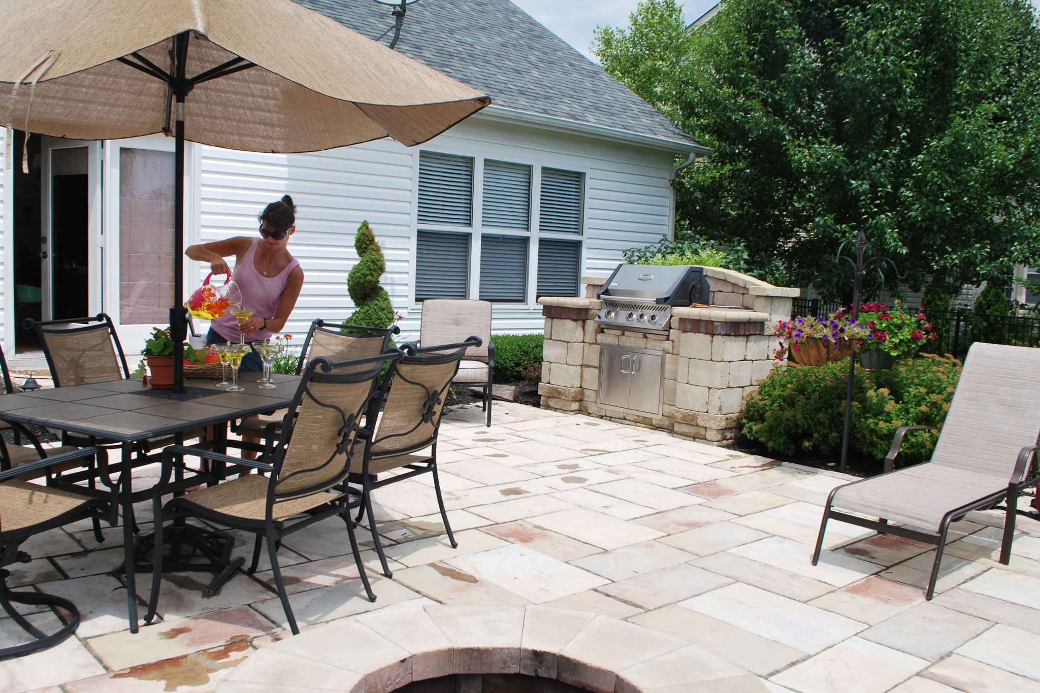 Woman pouring drinks on backyard patio with grill 