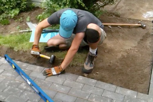 Man with knee pads and gloves installing pavers with hammer