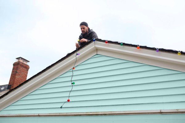 Man on roof hanging string of multi-colored Christmas lights