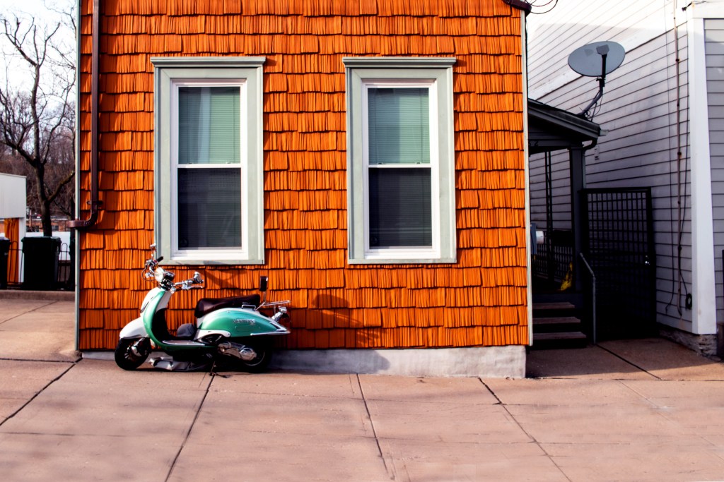 Wood-paneled house with green scooter resting against it