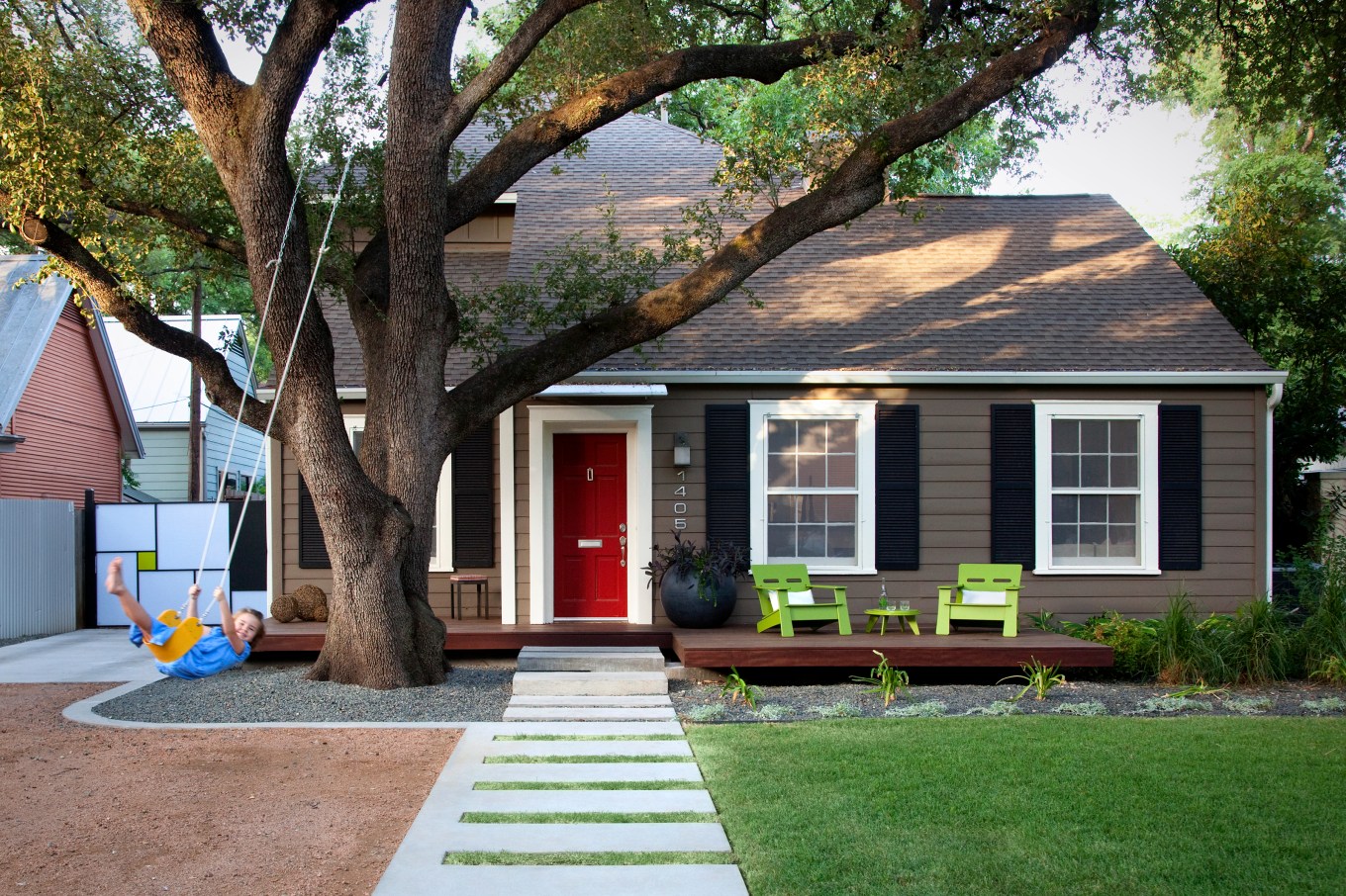 Gray house with green deck chairs and child on swing