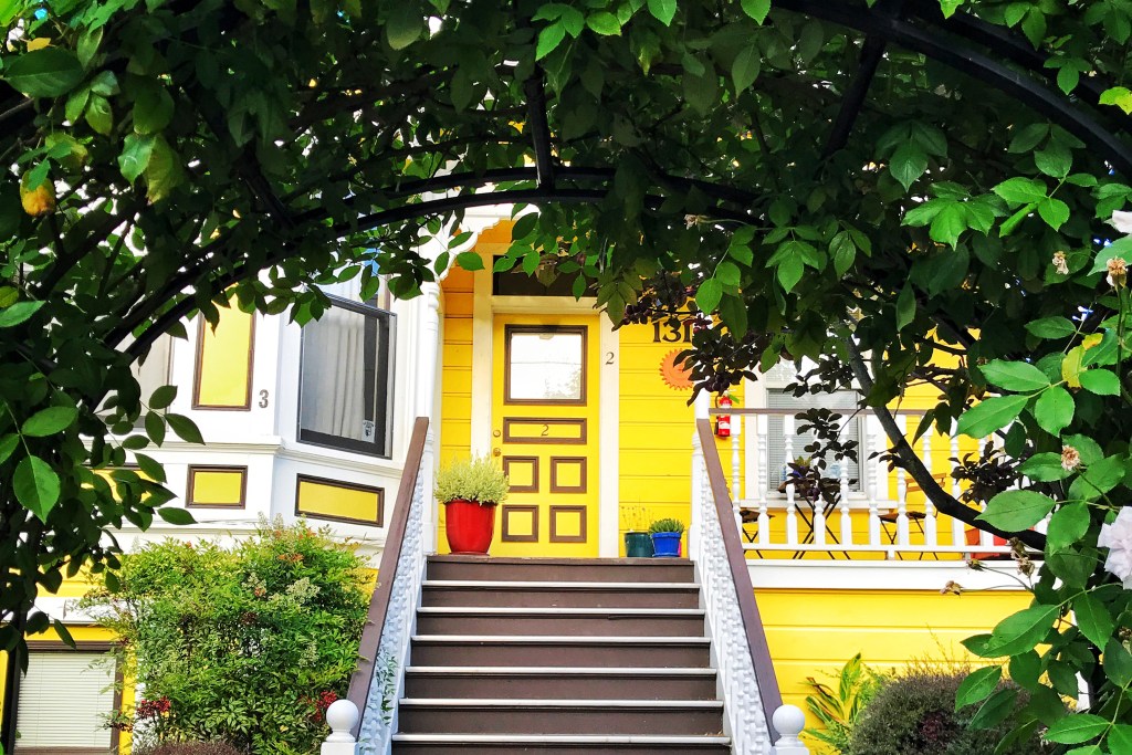 Foliage archway framing front steps and yellow door