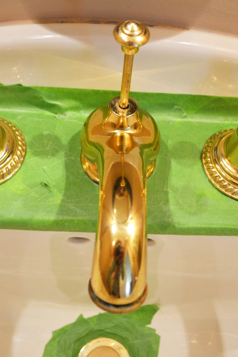 A brassy faucet with green painter's tape in a bathroom