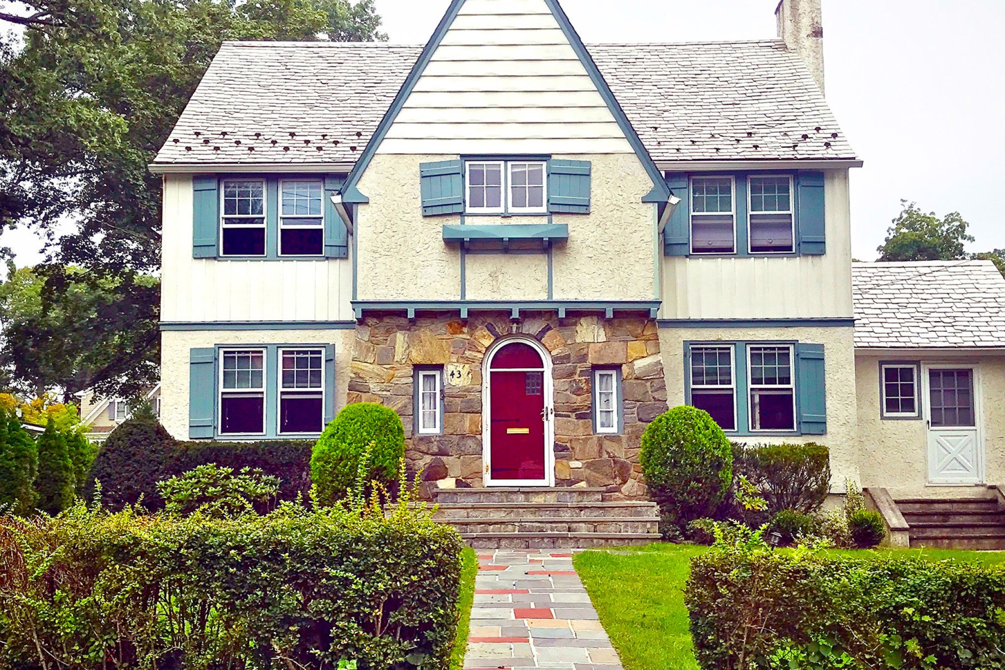 Two-story white tudor with blue trim and stone facade