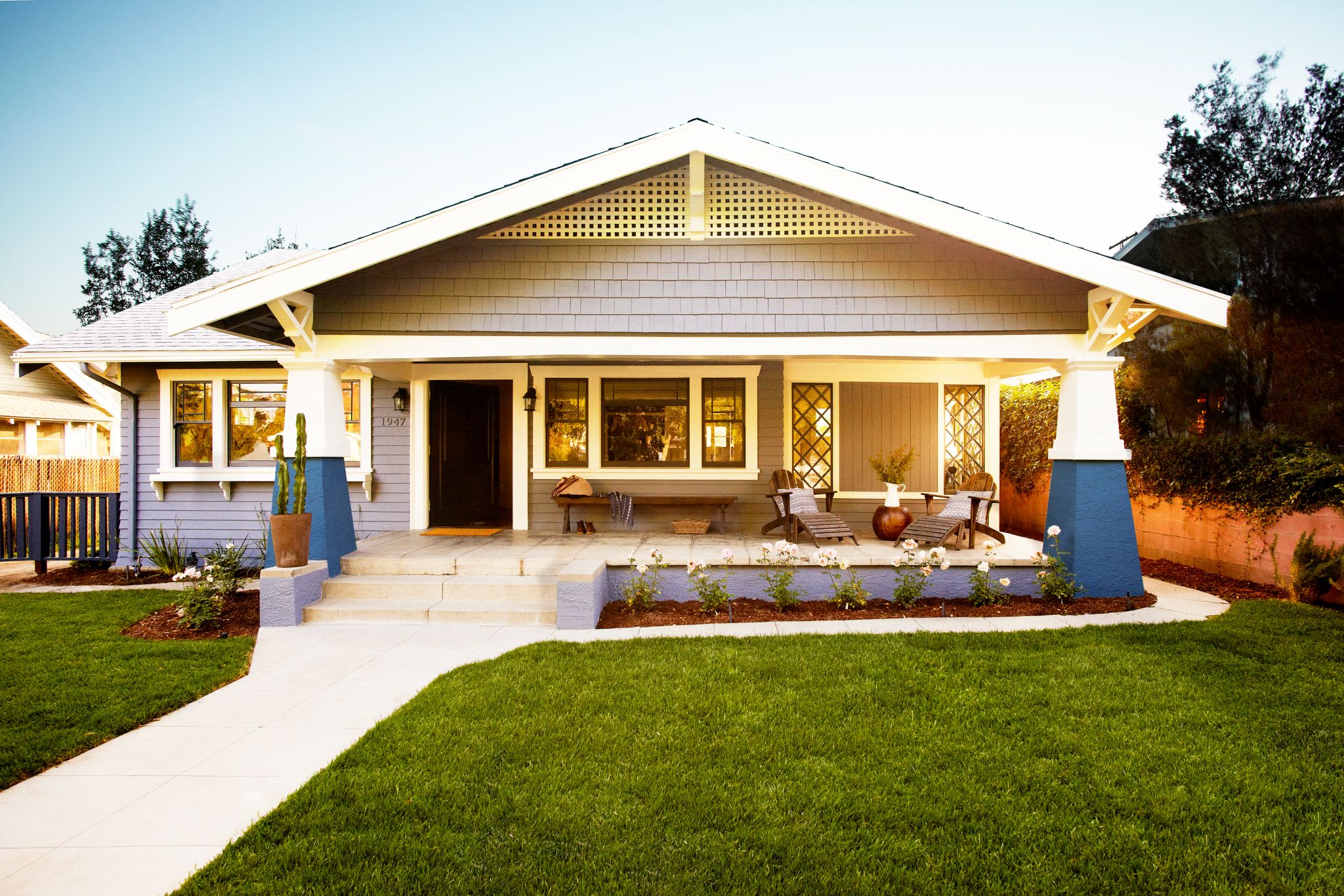 Front view of a cozy bungalow with yard and porch at dusk