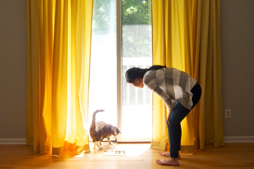 Woman and her cat standing in front of sunny yellow curtains