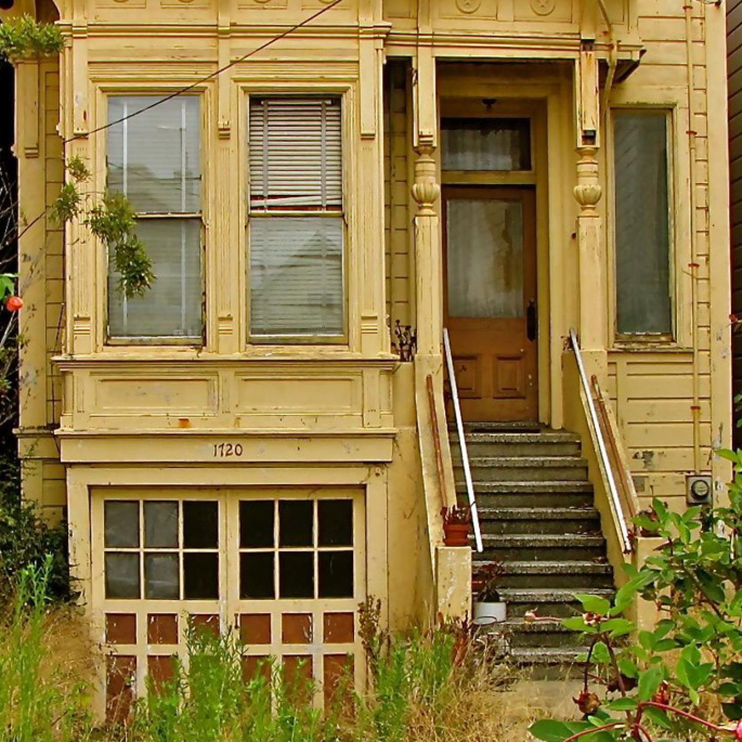 Dilapidated home exterior with overgrown weeds