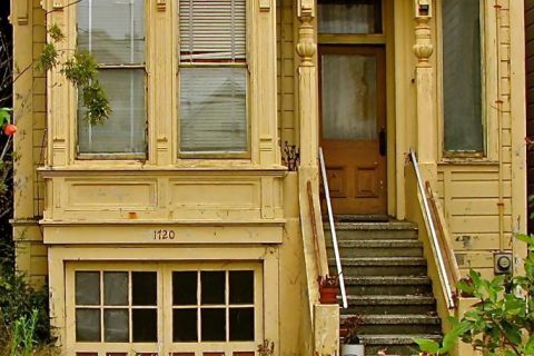 Dilapidated home exterior with overgrown weeds