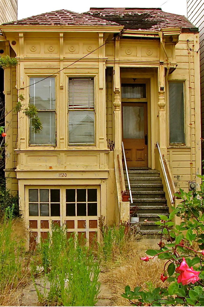 Dilapidated home exterior with overgrown weeds