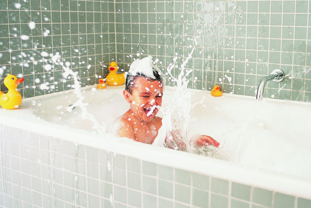 A young boy in a bath tub surrounded with bubbles & ducks
