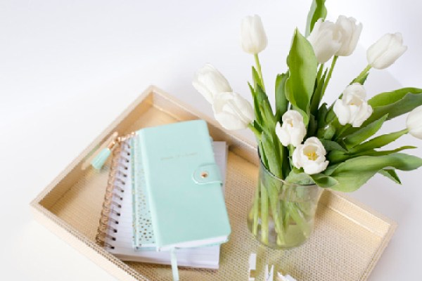 Mint notebooks on a gold tray with a vase of white tulips