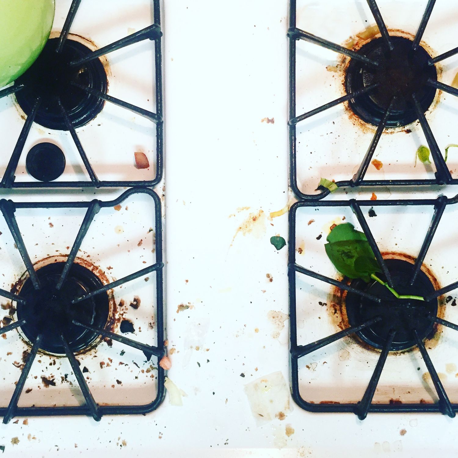 A gas stovetop with food crumbs, green teapot