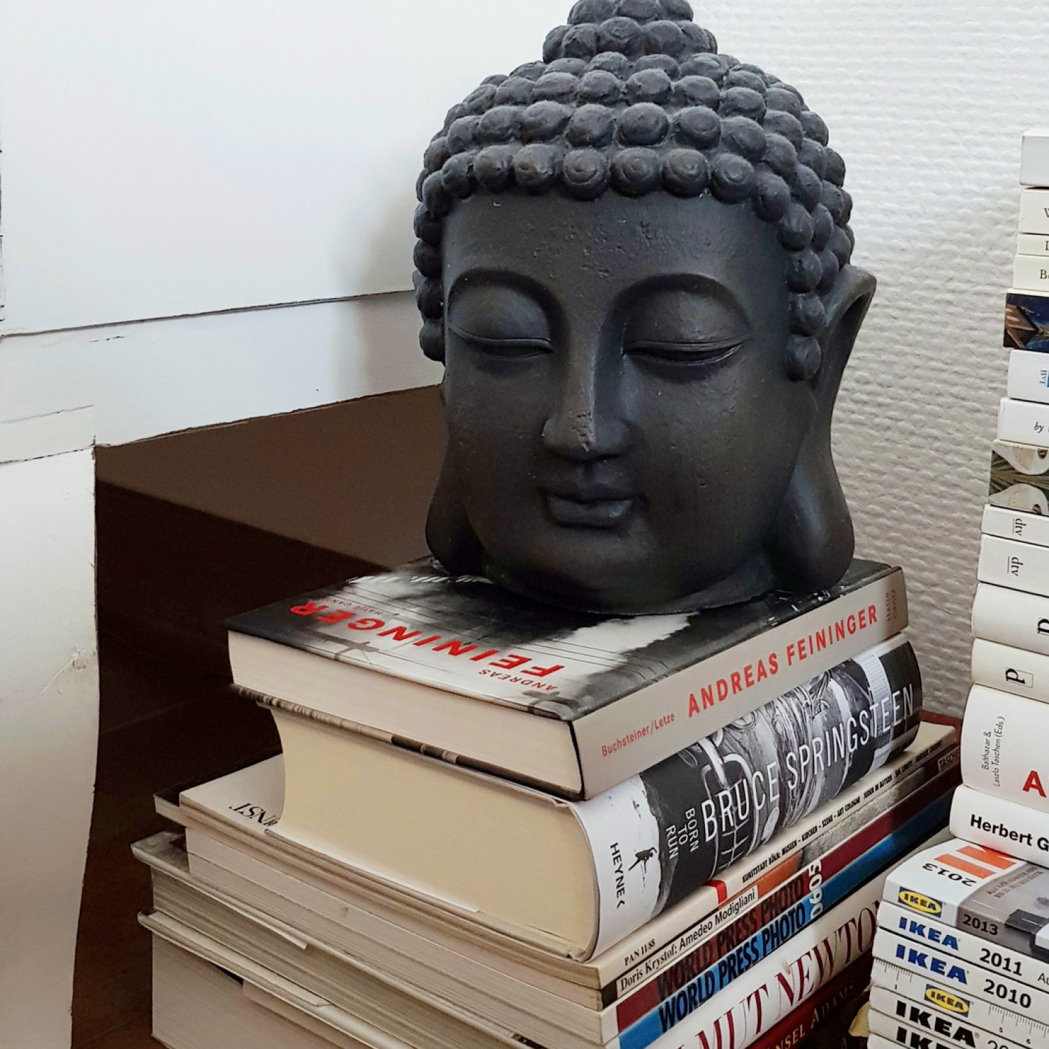 A gray buddha statue on a stack of white books, catalogs