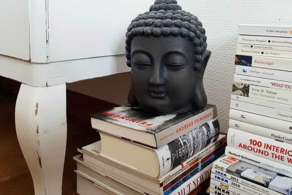 A gray buddha statue on a stack of white books, catalogs