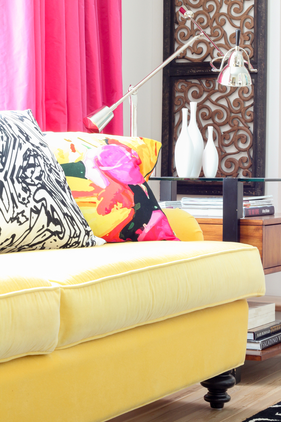 A close-up of a yellow couch, pink curtains, & floral pillow
