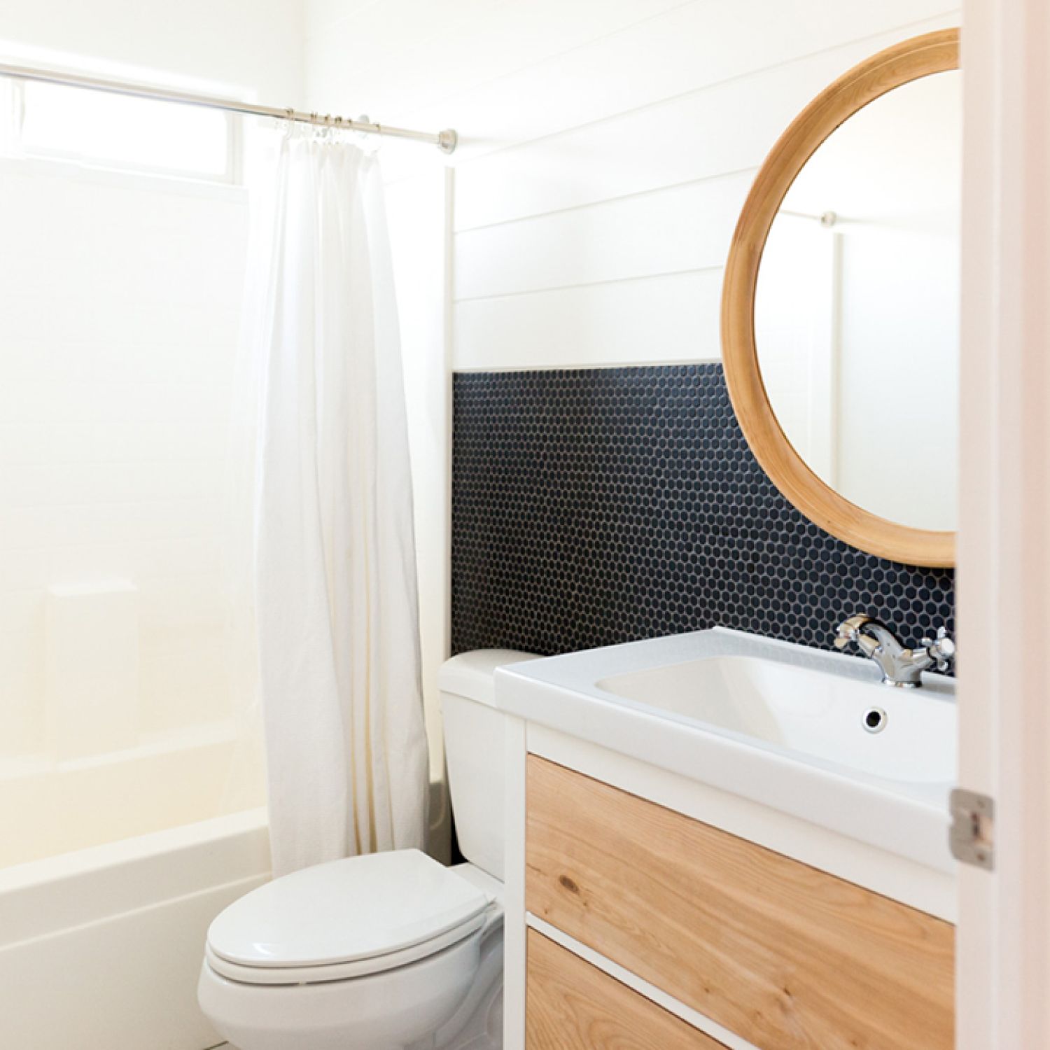 A white bathroom with black tile and natural wood accents