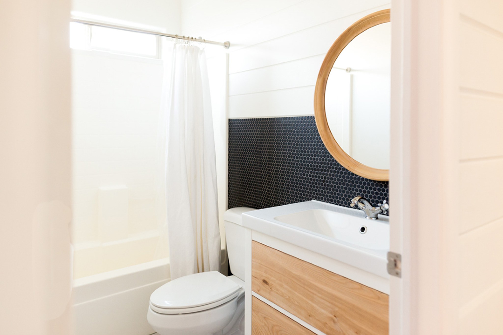 A white bathroom with black tile and natural wood accents