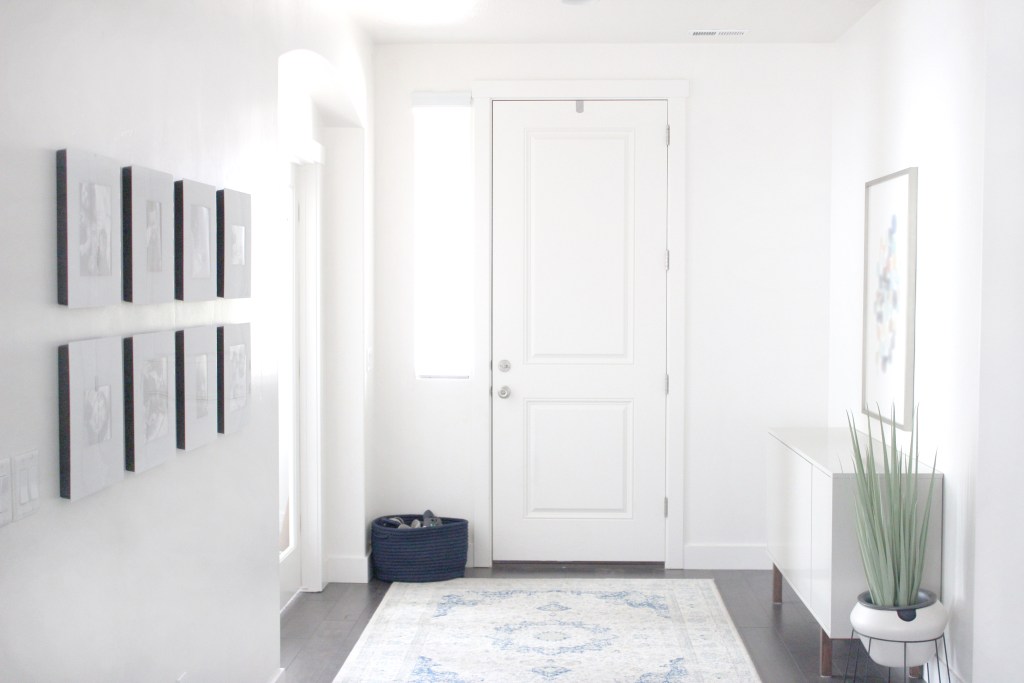White entryway with pictures along one wall and white rug