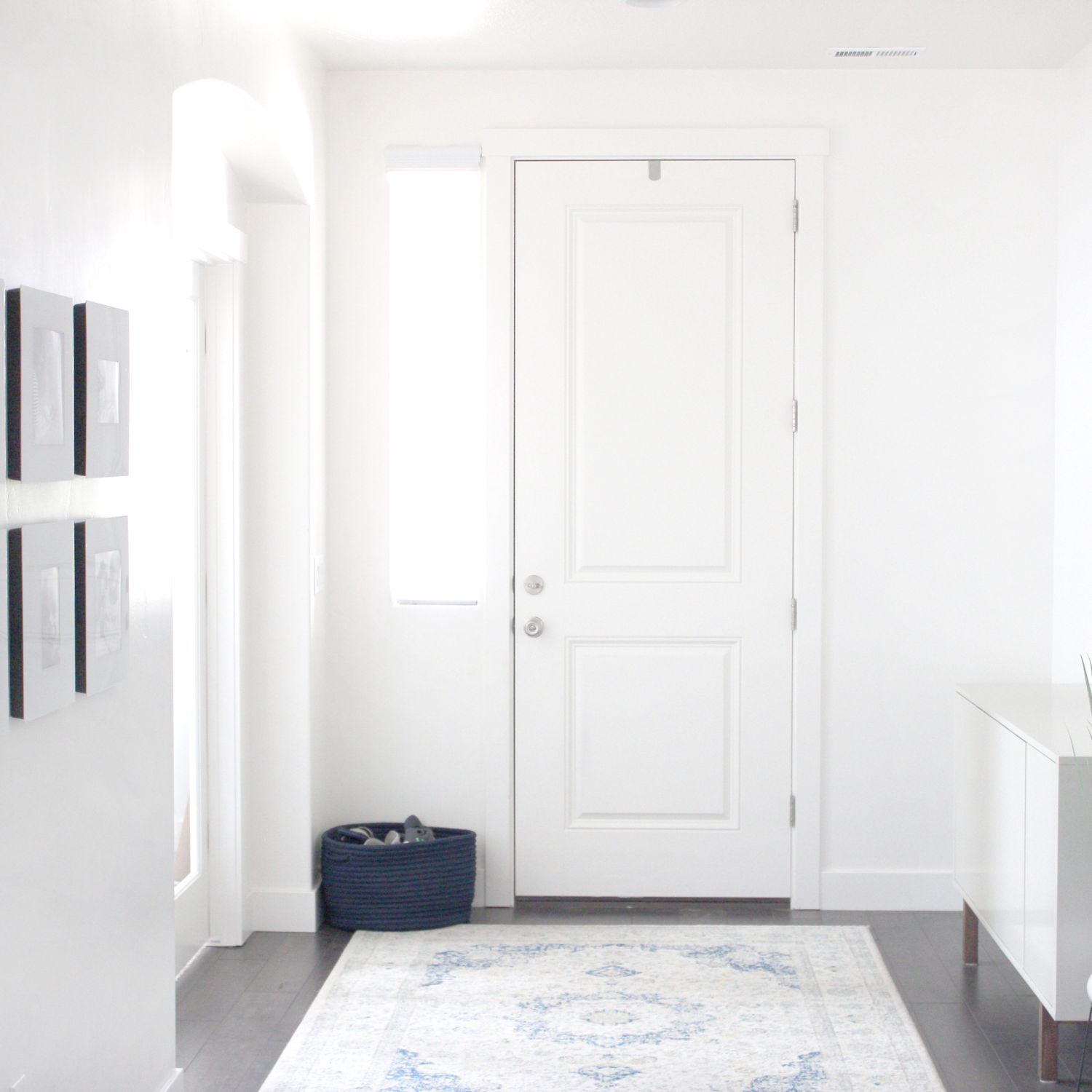 White entryway with pictures along one wall and white rug