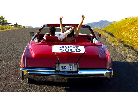 Couple in red convertible with "just sold" sign on trunk