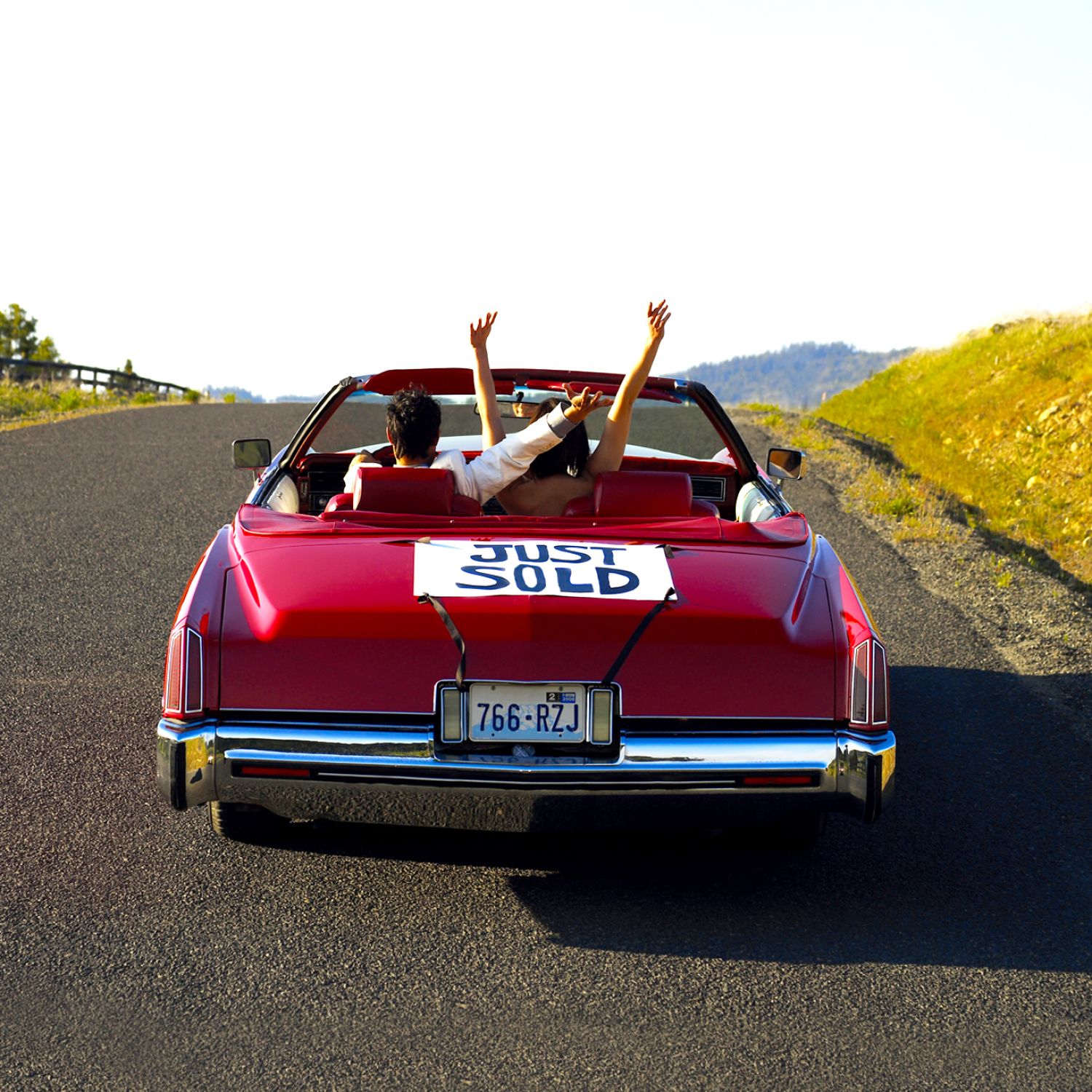 Couple in red convertible with "just sold" sign on trunk