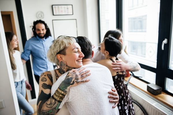 Women with short blond hair and tattoos hugging house guests