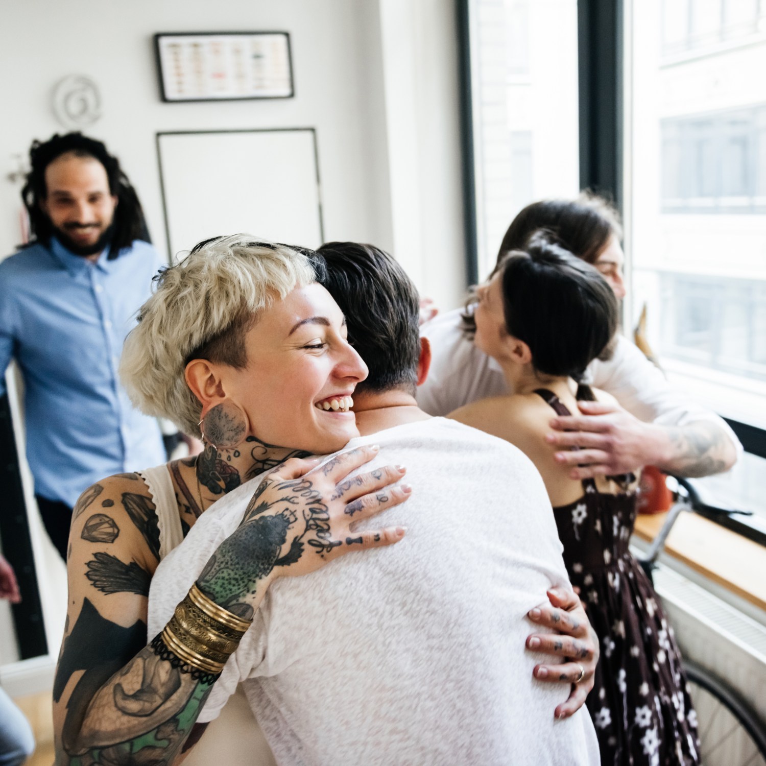 Women with short blond hair and tattoos hugging house guests