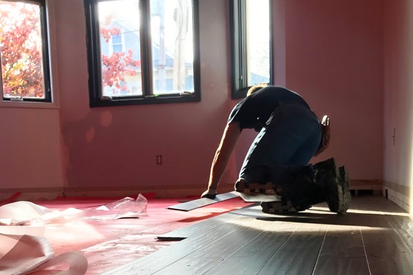 Man on hands and knees laying boards for wood floor