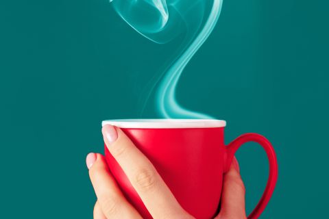 Hand holding red mug with heart-shaped smoke from beverage