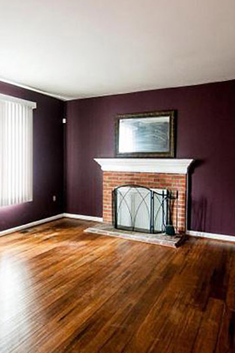 Empty room with purple walls, wood floor and brick fireplace
