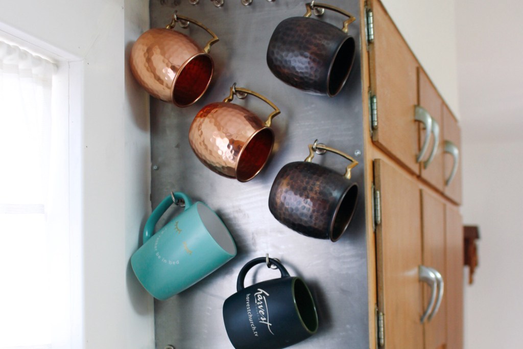 Assorted copper and ceramic mugs hanging on side of cabinet