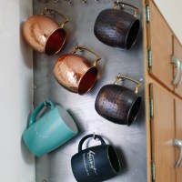 Assorted copper and ceramic mugs hanging on side of cabinet