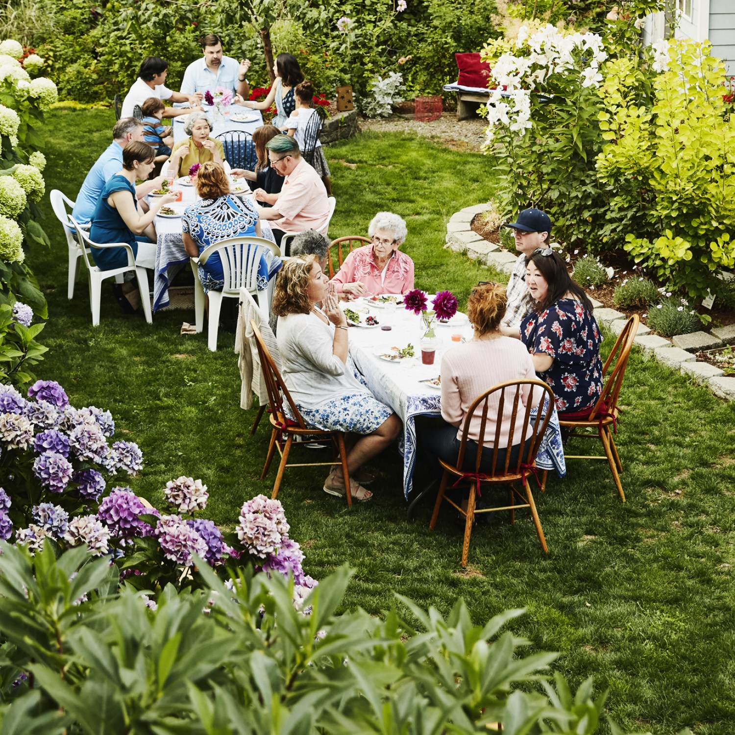 Families gathered at two tables enjoying time in backyard