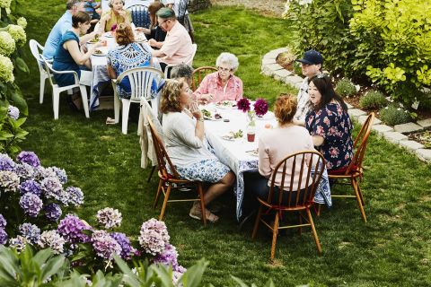 Families gathered at two tables enjoying time in backyard