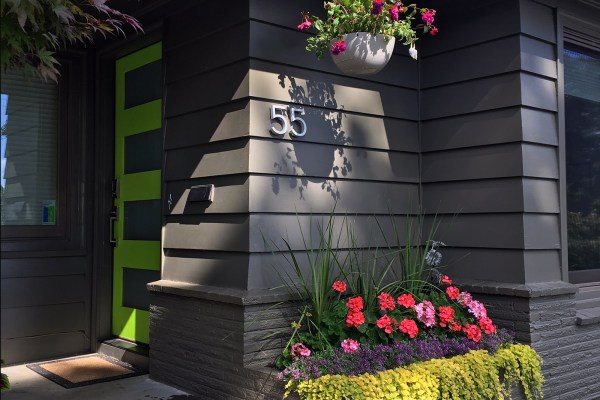 Dark gray house with lime green door and flower beds
