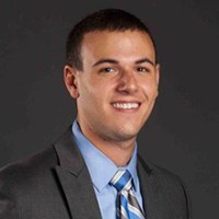 Photo of Daniel Bortz smiling in suit against gray backdrop