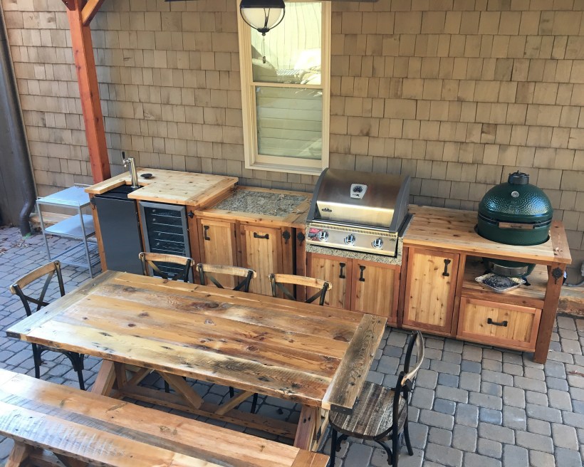 Wooden outdoor kitchen with grill, mini fridge, and table