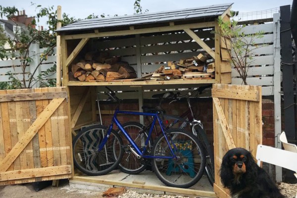 A residential backyard shed designed with areas for storing bikes and firewood.