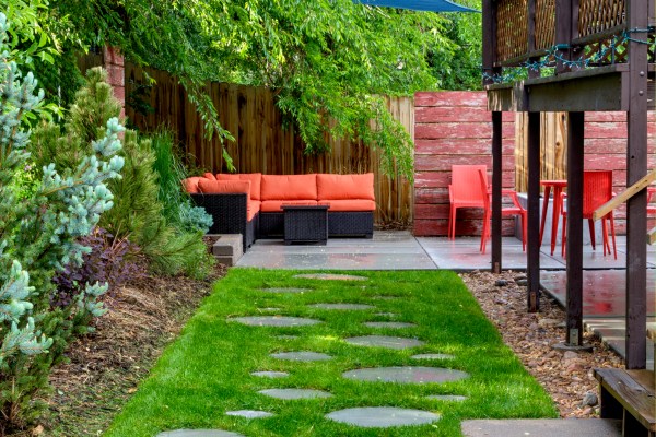 Bug free backyard patio has couch orange chairs blue shade sails a deck with paver walkway in grass
