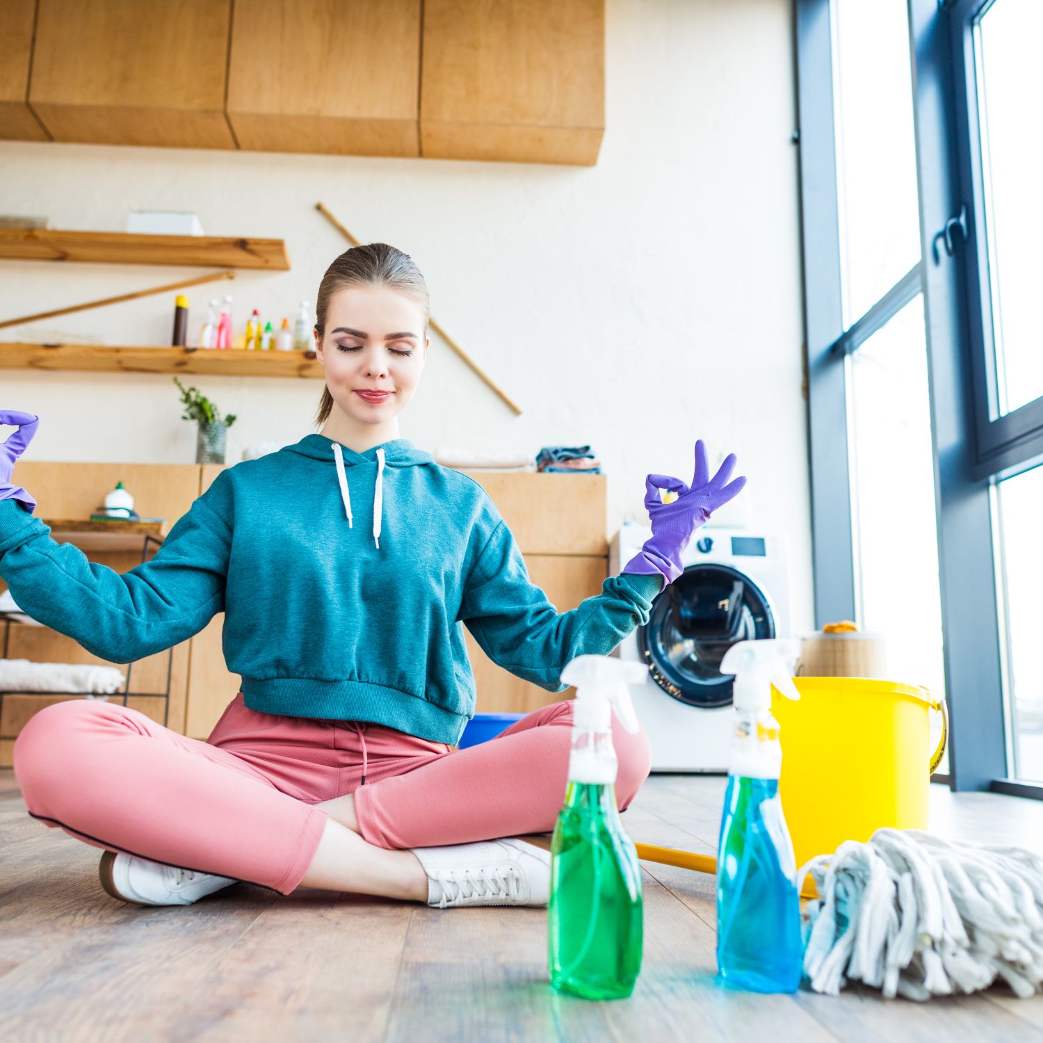 smiling young woman sitting on floor and meditating while cleaning house