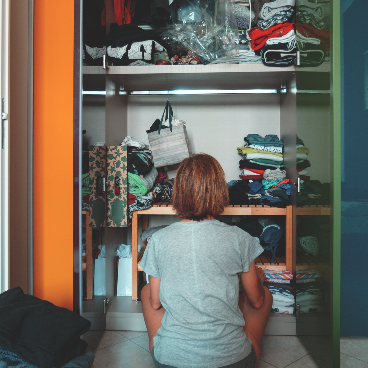 A woman sitting on the floor in front of a cluttered closet.
