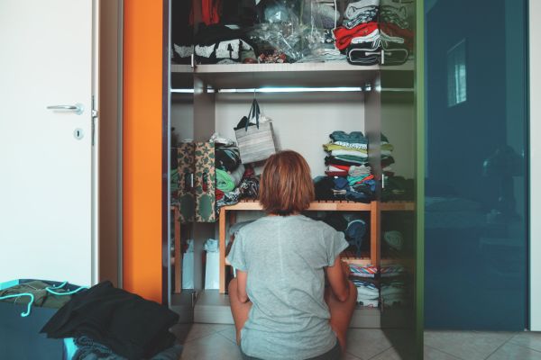 A woman sitting on the floor in front of a cluttered closet.