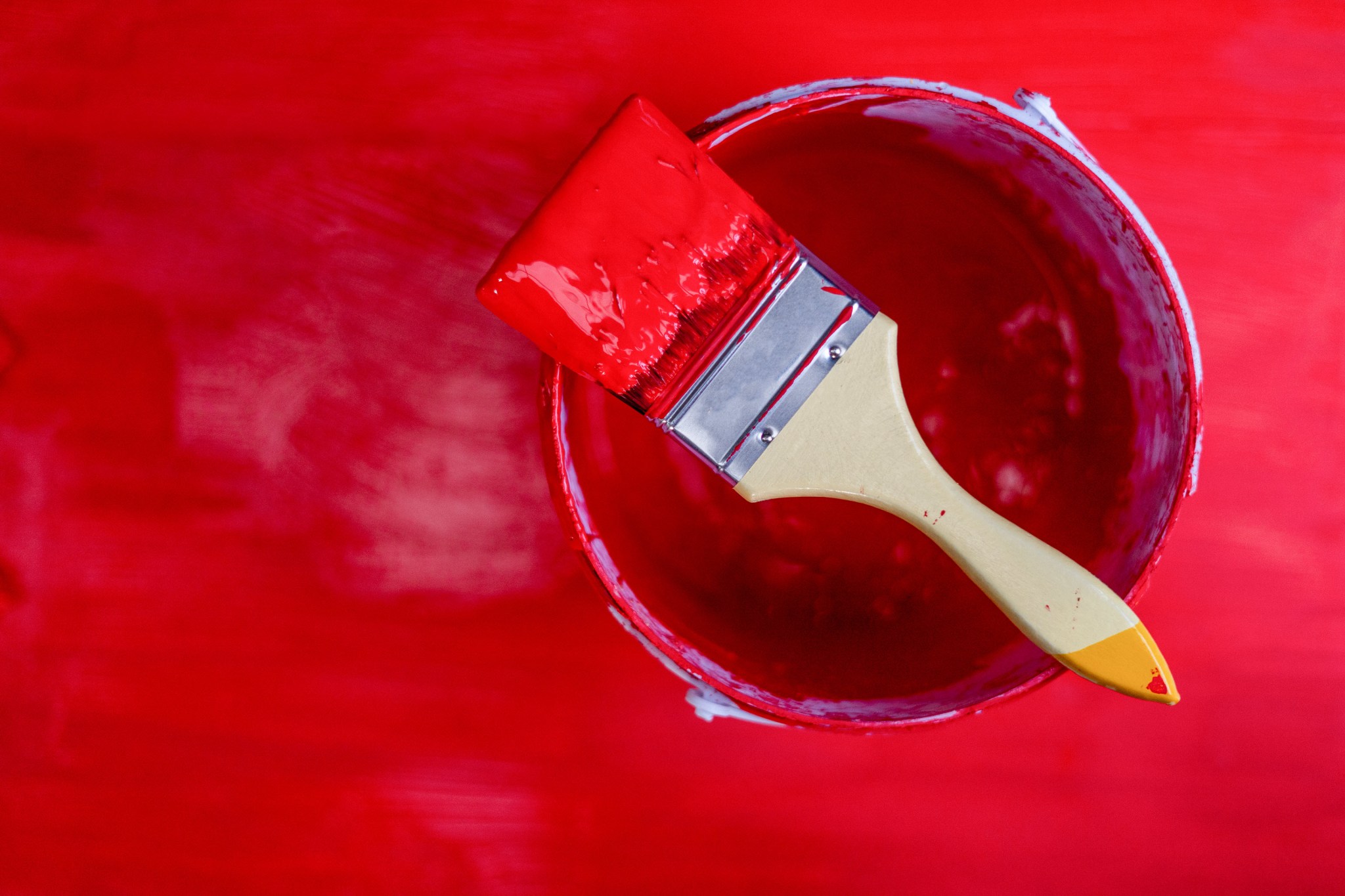 A paintbrush on a bucket filled with red paint.