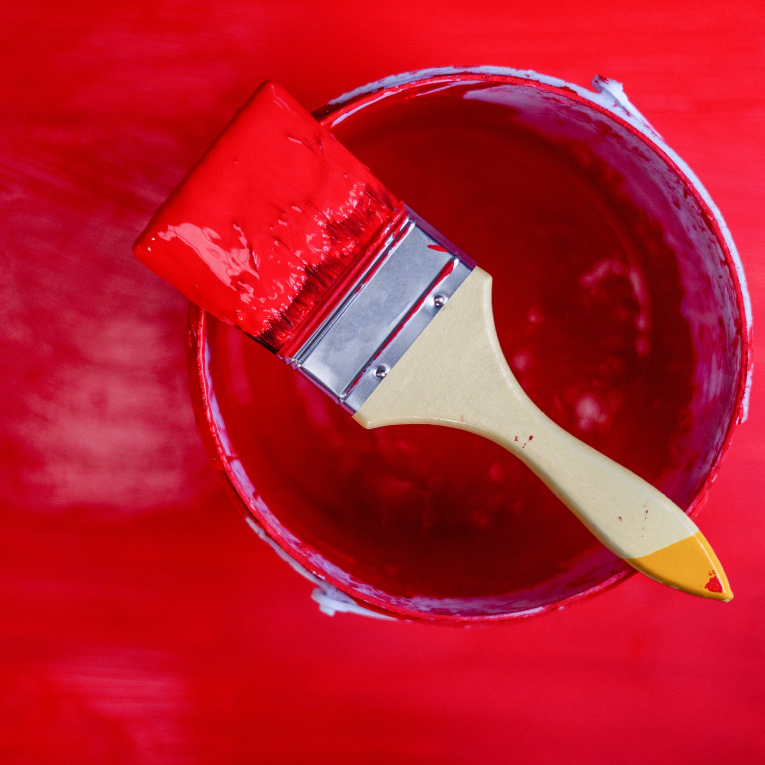 A paintbrush on a bucket filled with red paint.