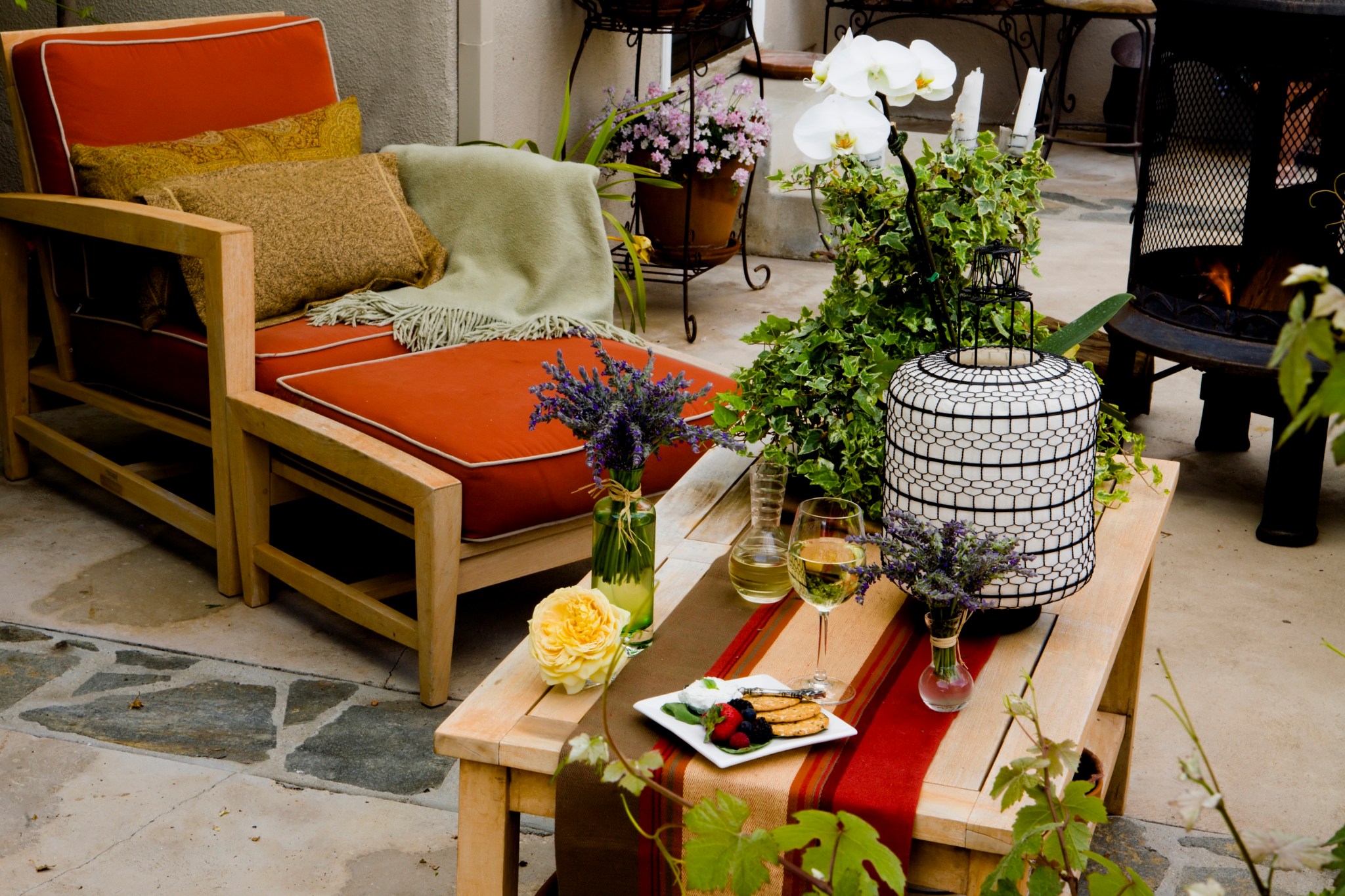 outdoor living space has colorful chair, ottoman and table next to fire pit and lots of plants on patio