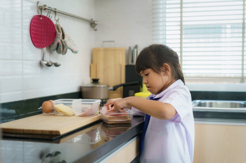 back to school organization young female student in a uniform making a sandwich for lunch box part of morning routine for school