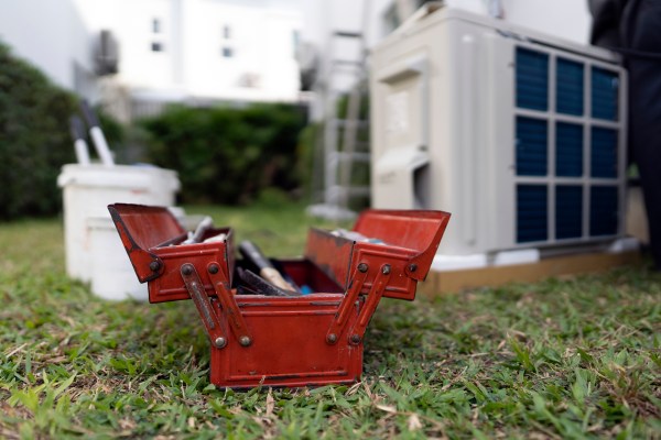when is it time to repair or replace appliances image of a vintage red metal toolbox on the grass in front of a broken air conditioner with a blurry background