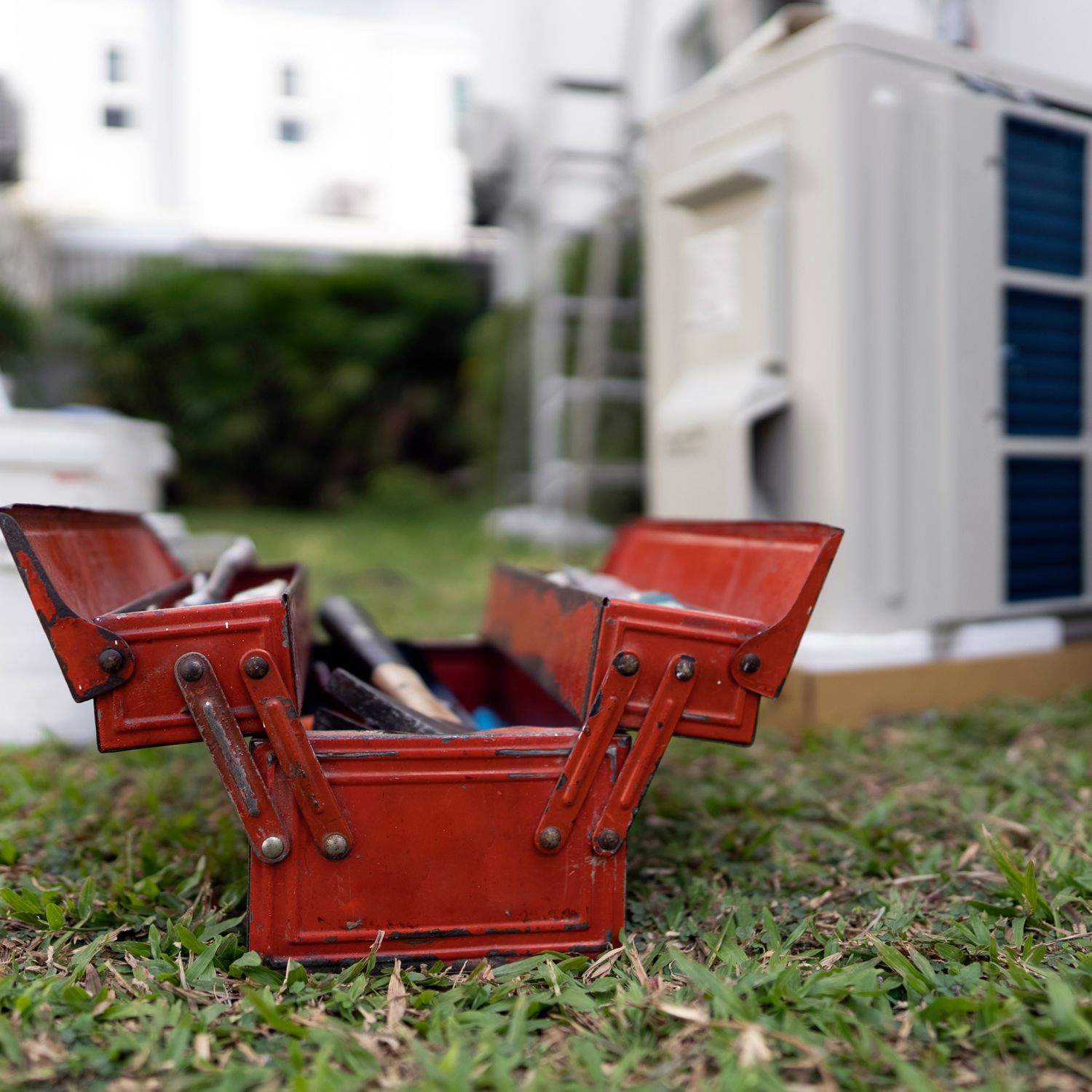 when is it time to repair or replace appliances image of a vintage red metal toolbox on the grass in front of a broken air conditioner with a blurry background