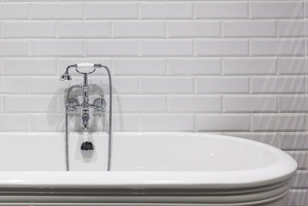 bathroom tile trends image of classic white subway tile in a bathroom with a white freestanding tub and a chrome faucet and handheld showerhead