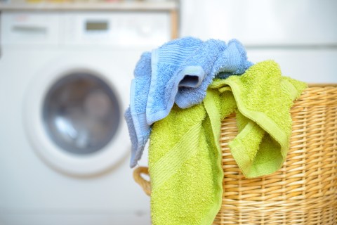 wicker laundry basket with dirty blue and green towels waiting for laundry with white washing machine in background